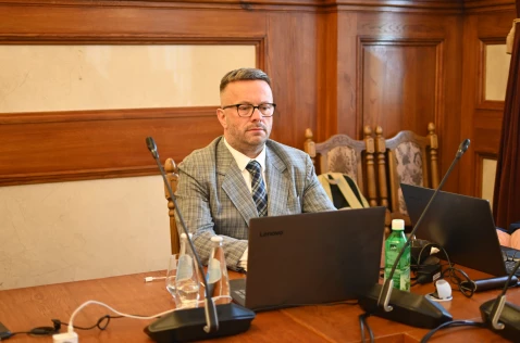 Radny Konrad Szymacha siedzi w sali sesyjnej przy laptopie