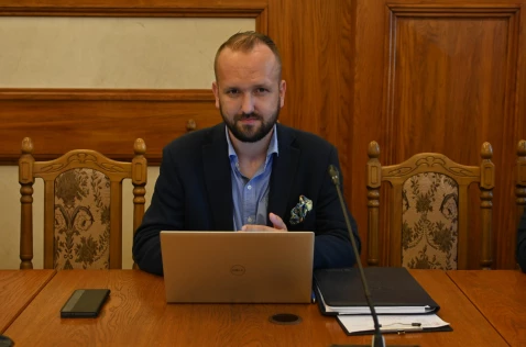 Radny Grzegorz Nędza siedzi przy laptopie w sali sesyjnej.