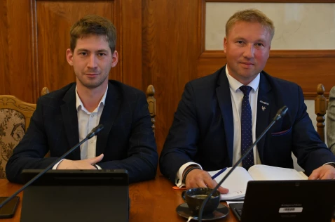 Radni Karol Pawełko i Bartłomiej Szczoczarz siedzą przy laptopach w sali sesyjnej.
