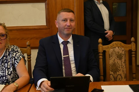 Radny Krzysztof Krupa siedzi przy laptopie w sali sesyjnej.