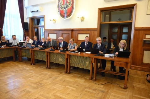 Radni Powiatu i skarbnik siedzą przy biurkach w sali sesyjnej. W tle siedzą 2 pracownicy Starostwa.